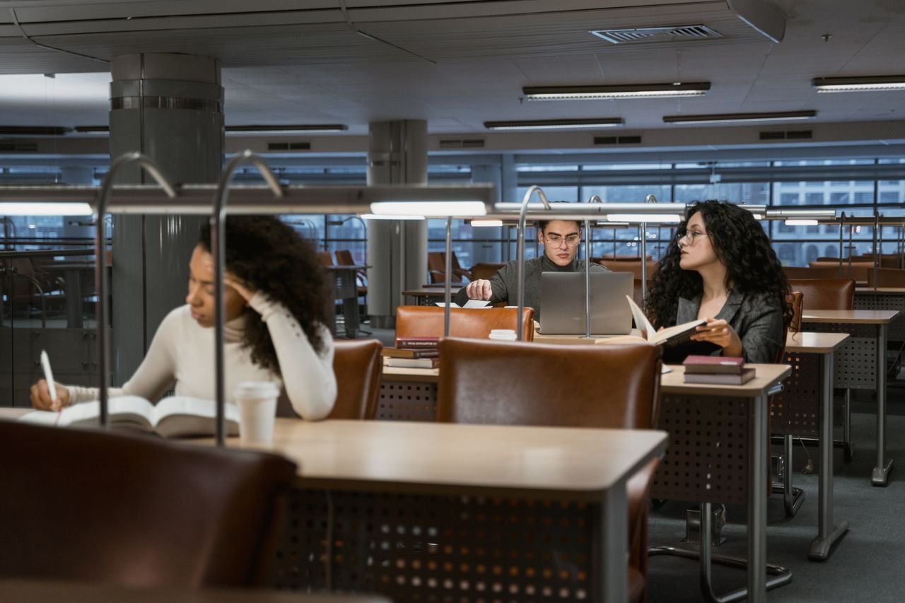 about-us College students studying in a modern library setting, concentrating on books and laptops.