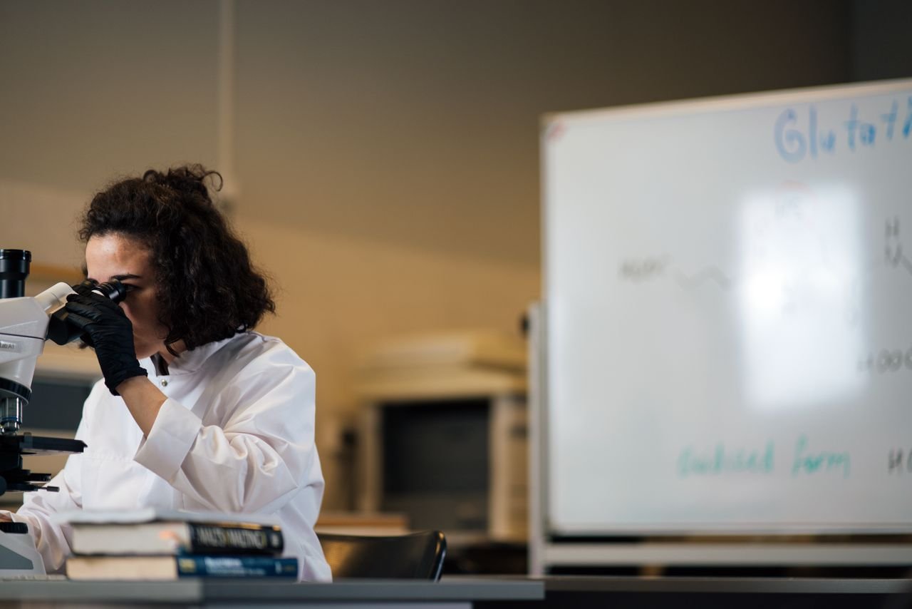 home-hero Female scientist examining samples under a microscope in a laboratory setting.